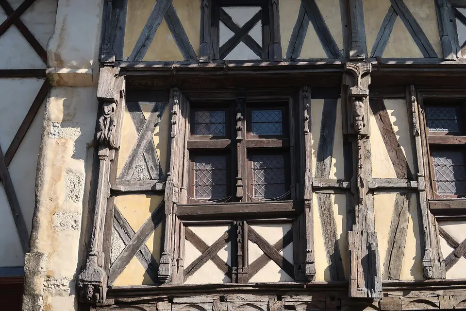 Détail d'une maison à pans de bois à Sainte-Foy-la-Grande, avec fenêtres en bois à petits carreaux insérées dans une façade à colombages sculptés.