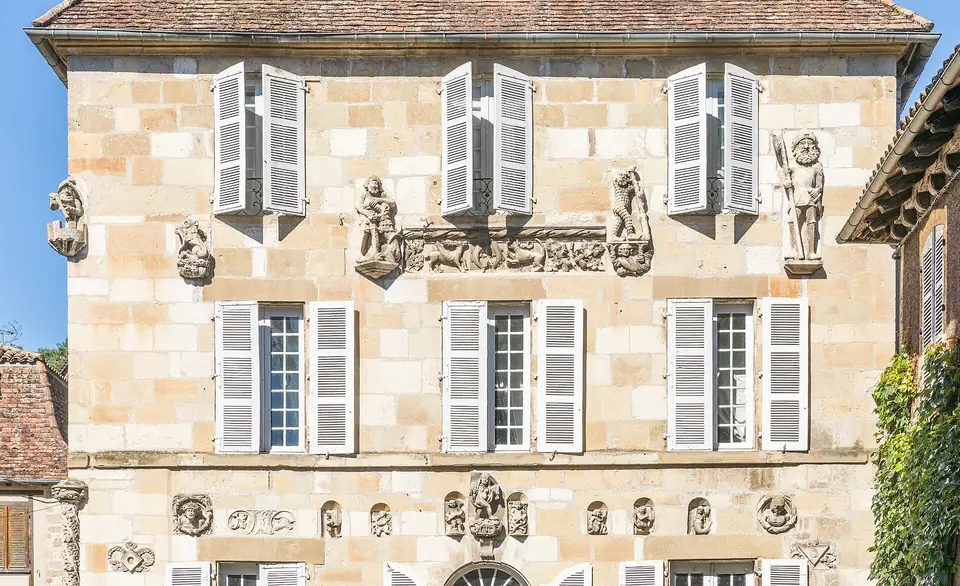 Façade de la maison Renaissance de Beaulieu-sur-Dordogne en pierre blonde, avec fenêtres à volets persiennés et frises de médaillons sculptés.