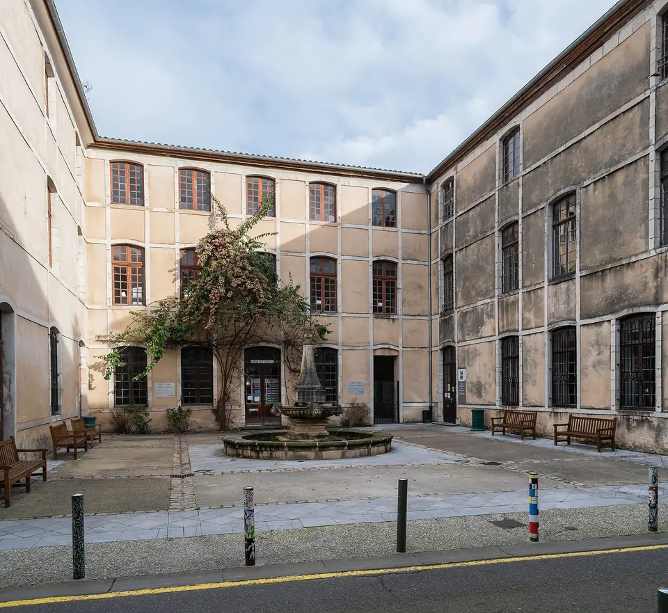 Cour d'un immeuble en pierre de la rue du Palais à Dax, façades percées de fenêtres régulières autour d'une fontaine.
