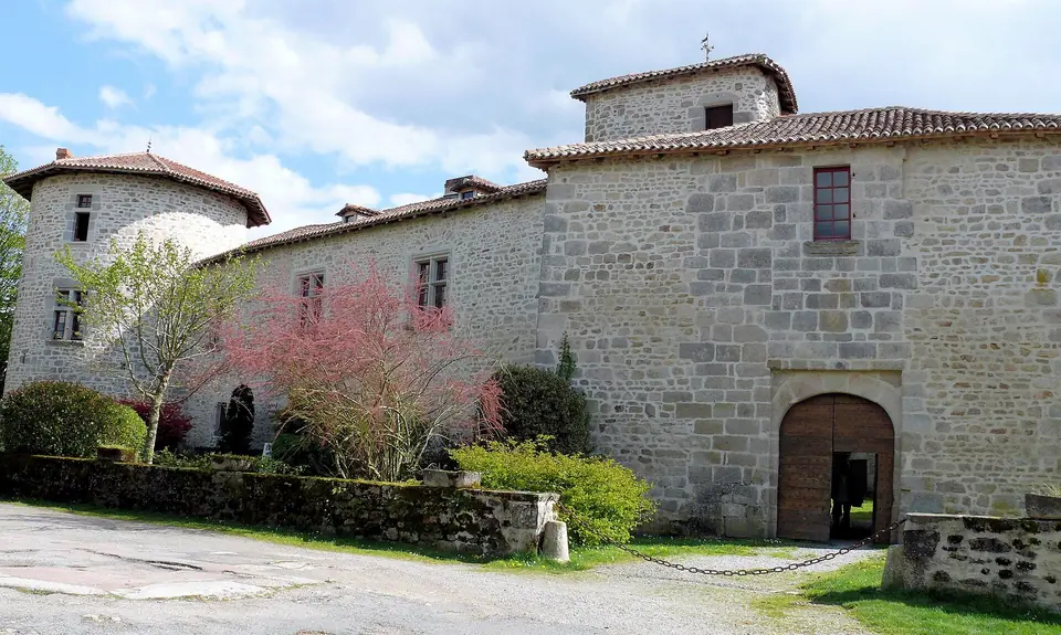 Château de Mortemart et dépendances en pierre, toits de tuiles et porte en bois, entourés d'arbres fleuris et de pelouse.